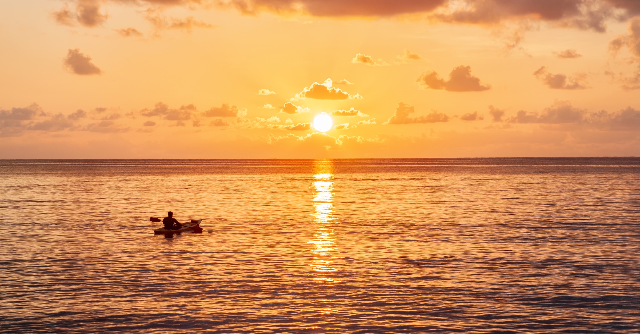Man paddling his kayak at sunset.