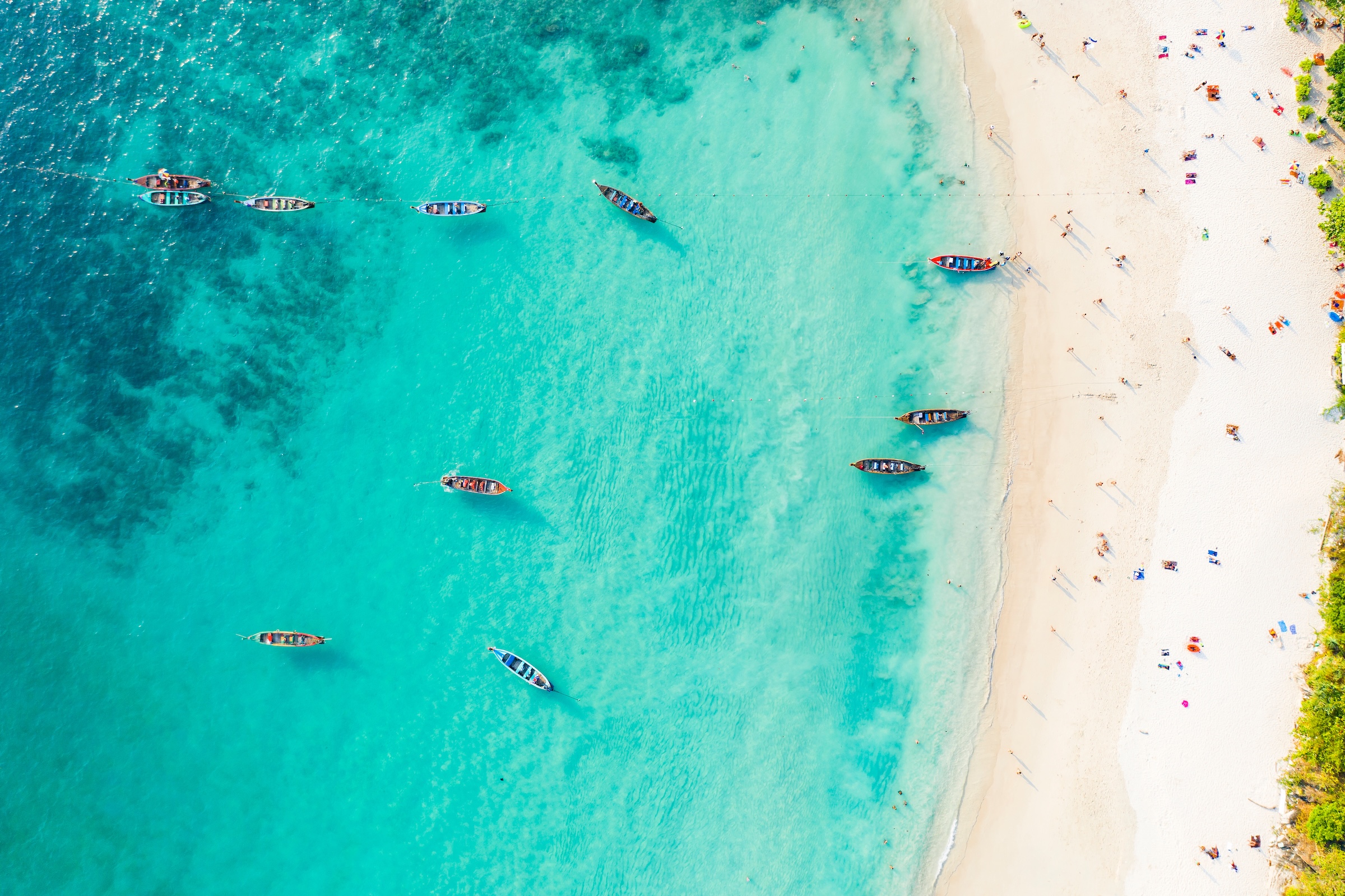 View from above, stunning aerial view of a beautiful tropical beach with white sand and turquoise clear water, long-tail boats and people sunbathing, Banana beach, Phuket, Thailand.